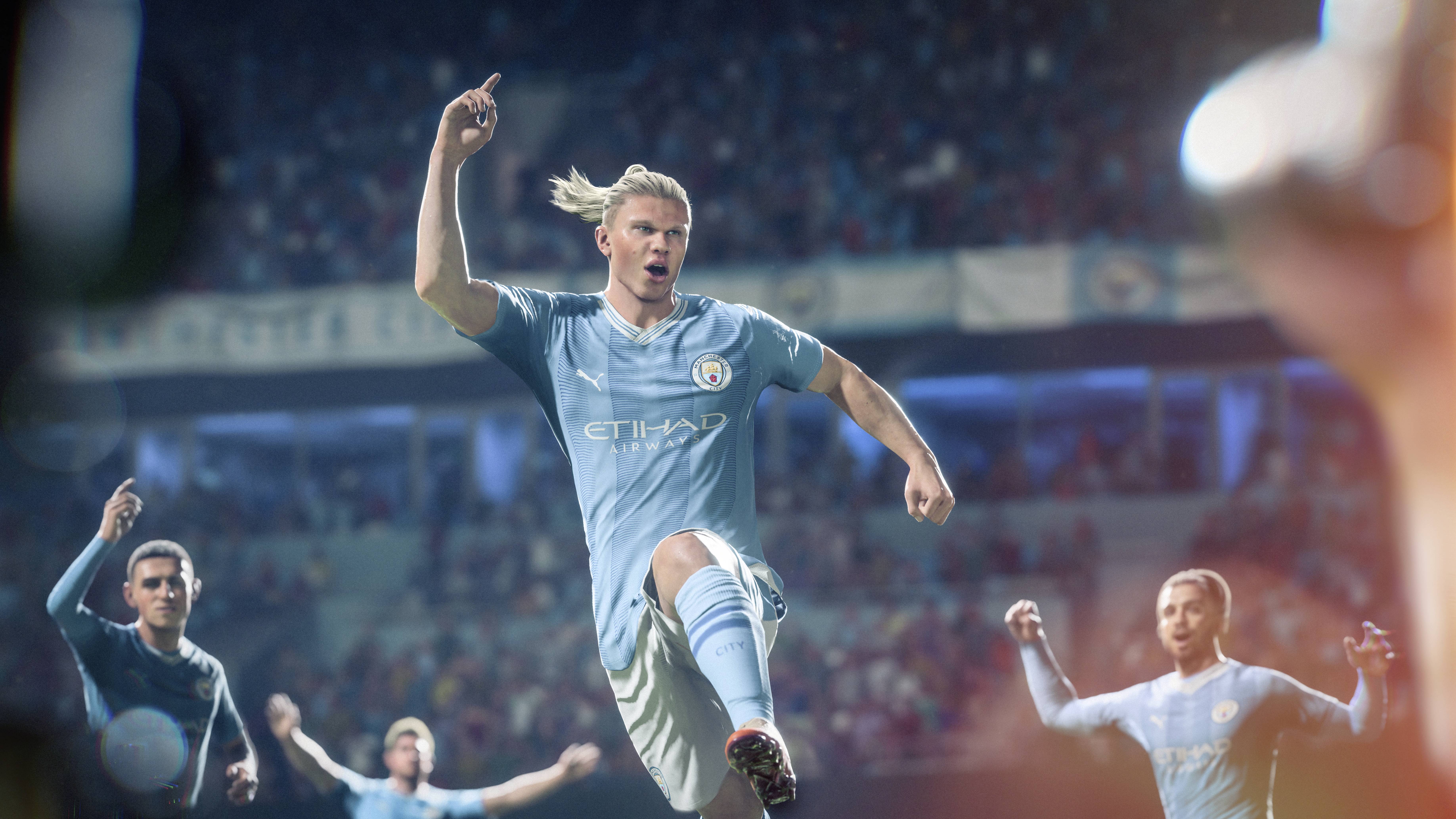 A footballer in a blue jersey is celebrating with his raised hand on the pitch, with cheering teammates visible in the background.