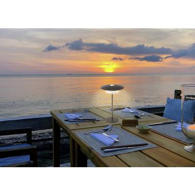 Dining table set for two with utensils and napkins, overlooking a serene ocean sunset with an orange glow reflecting on the water.