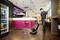 A man is cleaning the floor of a modern bar with a floor cleaning machine. Colourful seating and an illuminated bar counter are visible in the background.