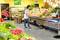A woman pulls a shopping trolley through the aisle of a greengrocer's shop. There is a wide variety of fresh produce.