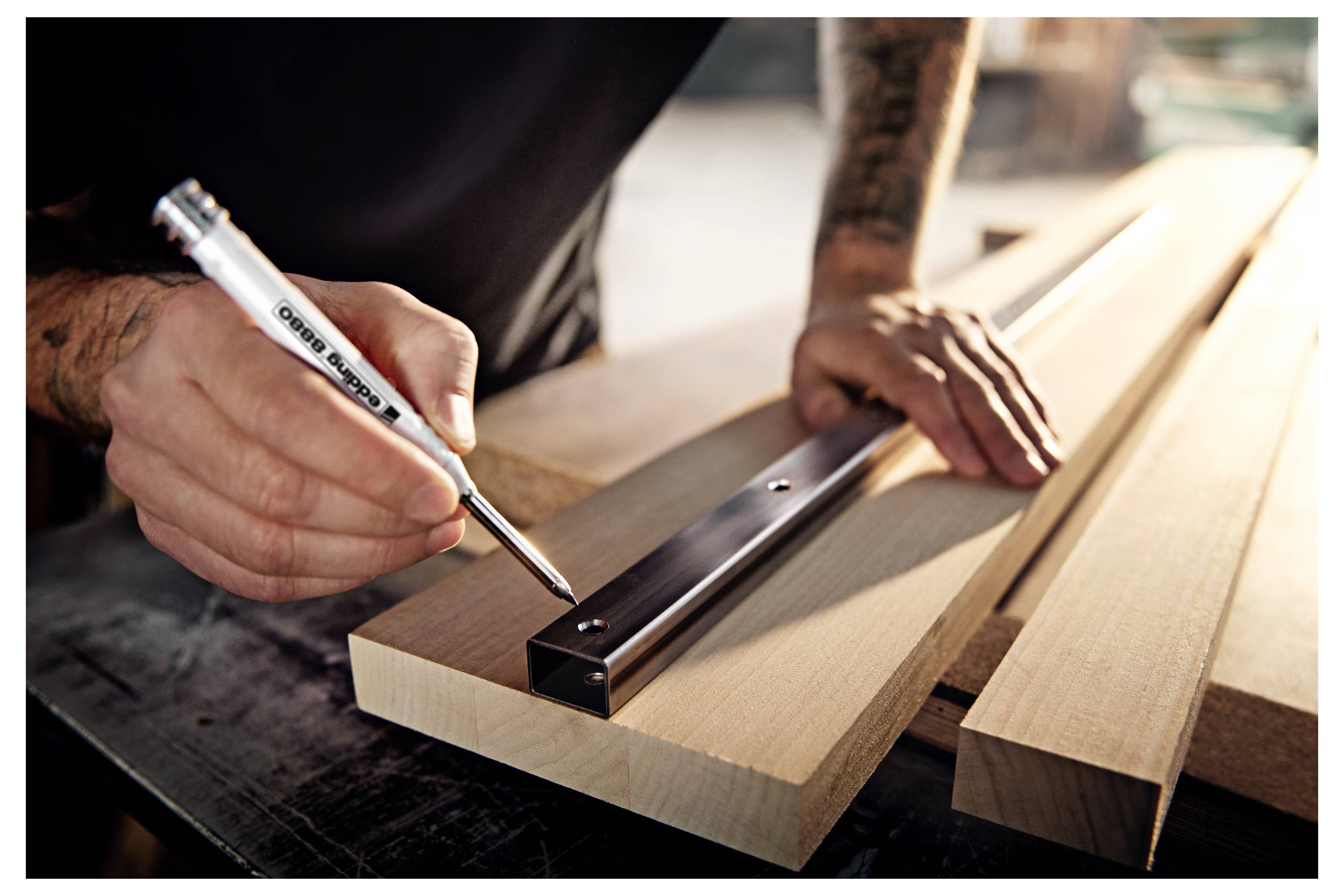 Close-up of a person marking a wooden board with a pencil beside a metal straightedge during carpentry work.