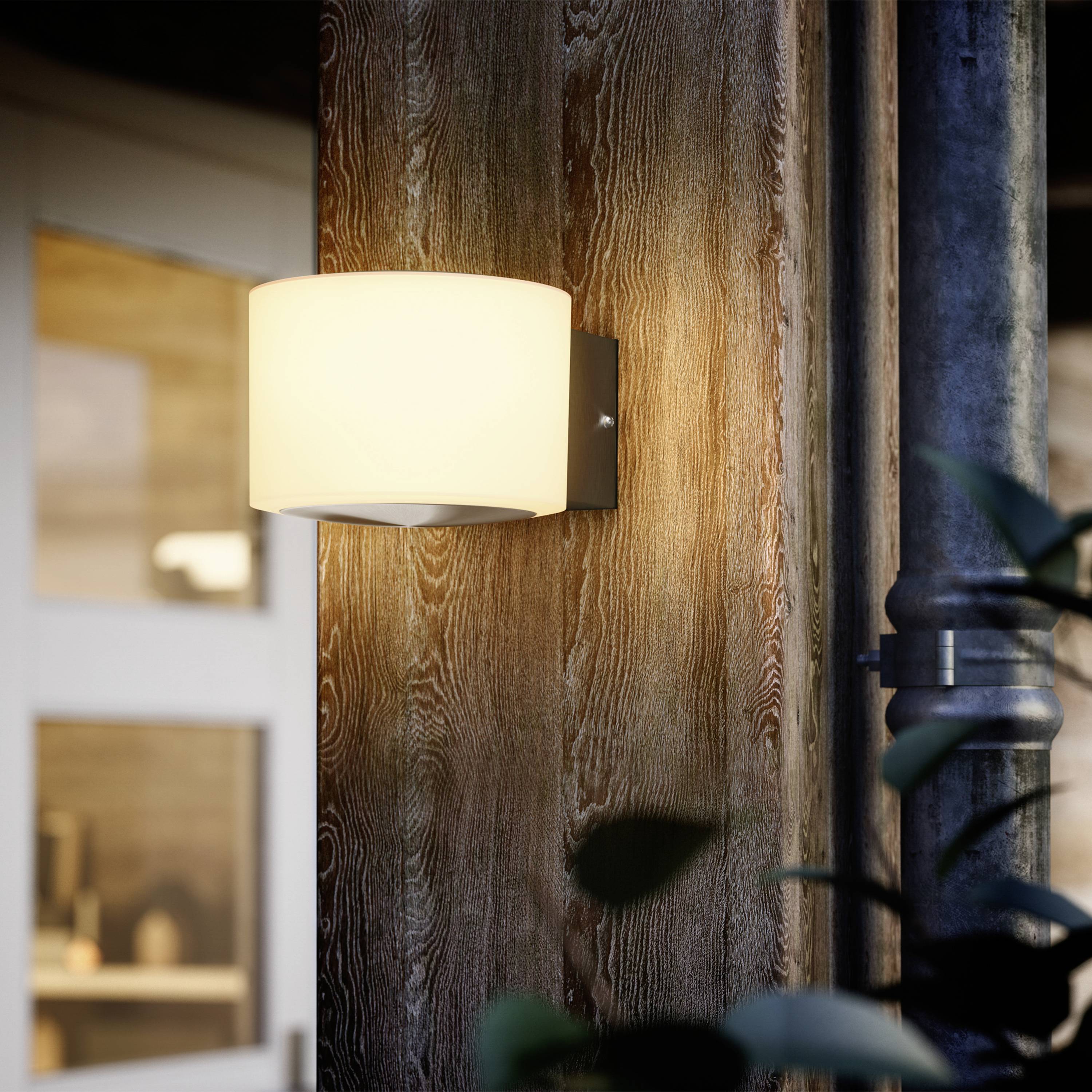 A contemporary wall light casts warm light onto a wooden wall in a cosy room with a visible window in the background.