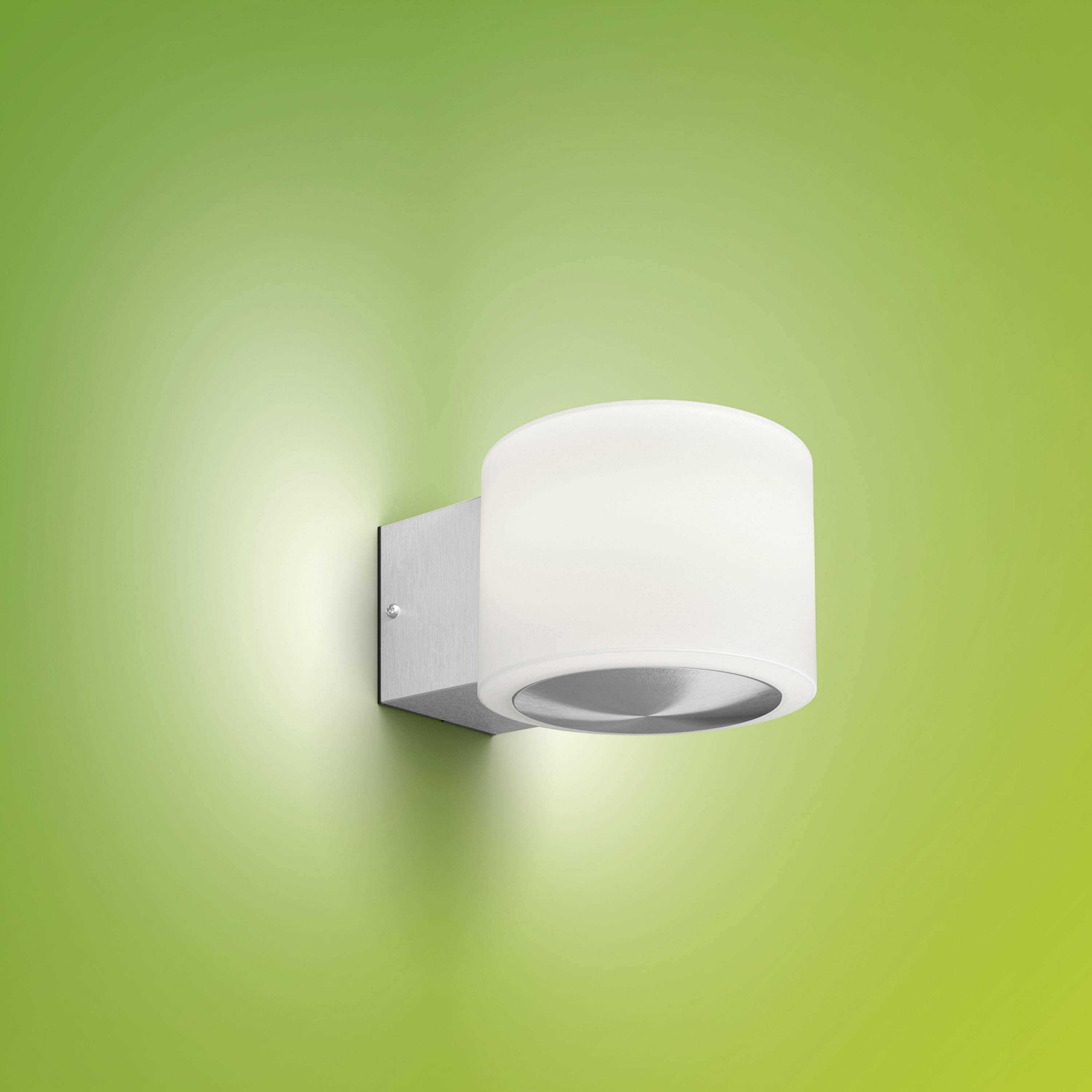 A modern wall light with a silver bracket and a cylindrical, white shade illuminates against a green background.