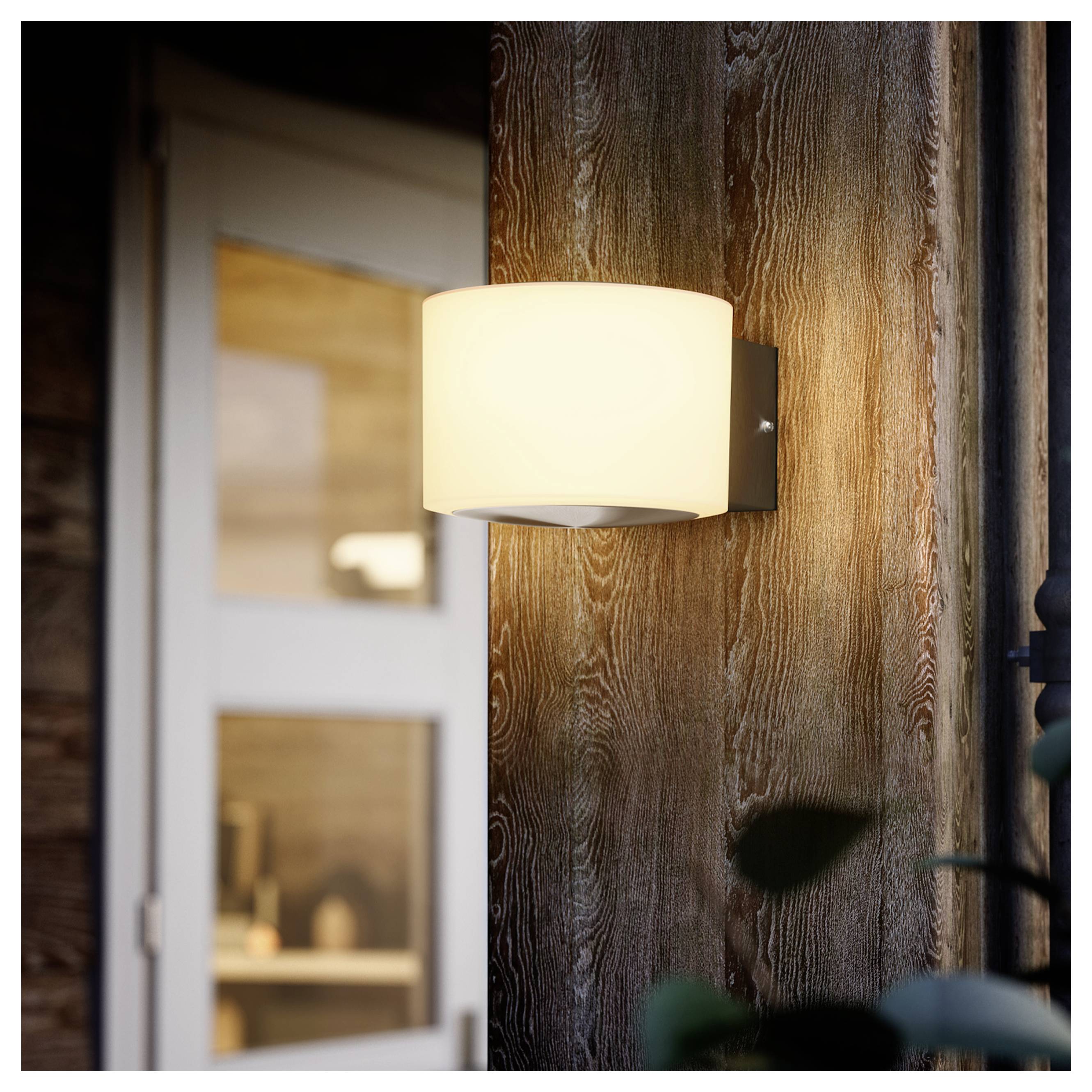 Wall-mounted outdoor light glowing on a wooden exterior wall beside a doorway.