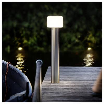 Modern outdoor lamp glowing on a wooden dock beside calm water at night, with a boat partially visible on the left.<br>