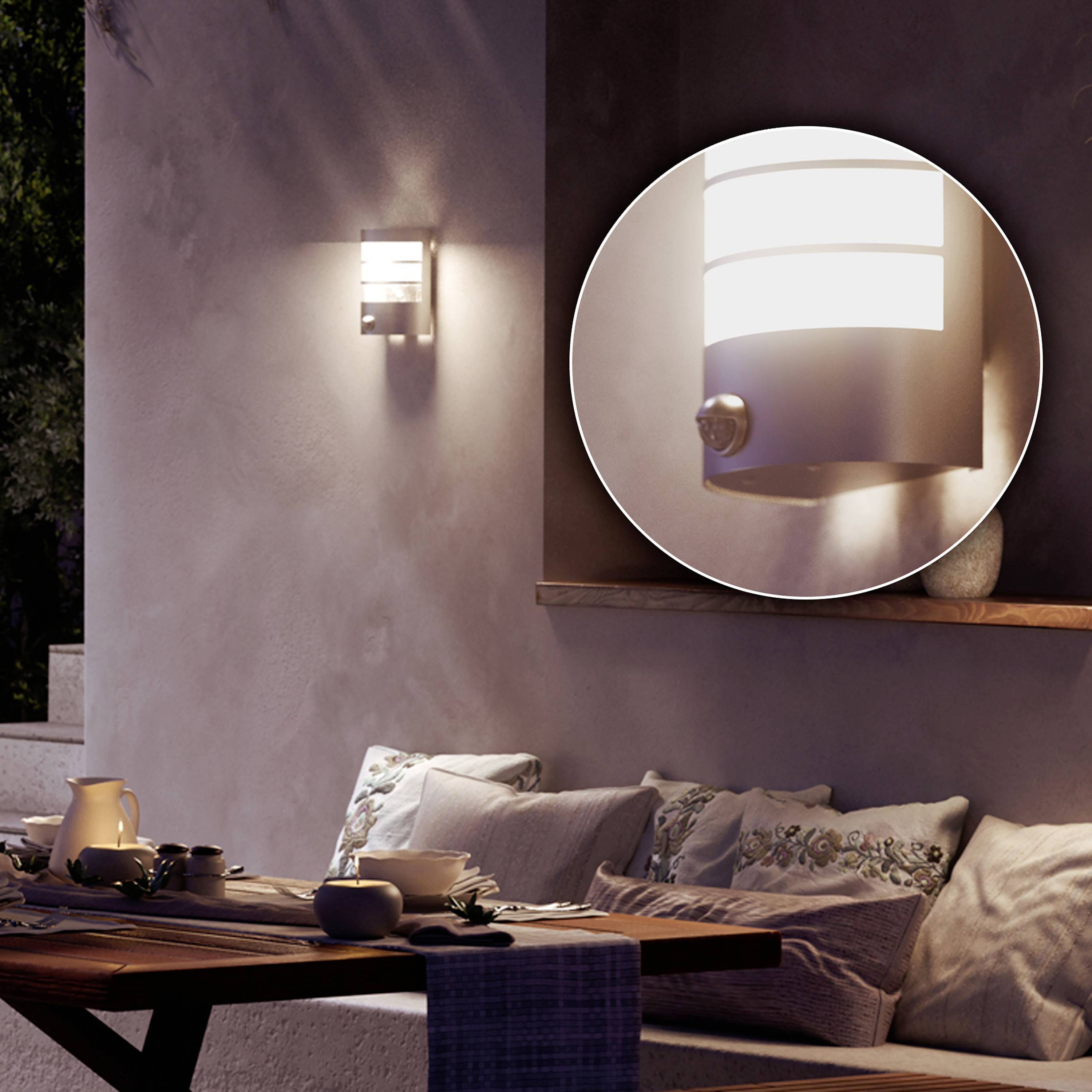 A terrace with a table, crockery and cushions. A modern outdoor light illuminates the wall.