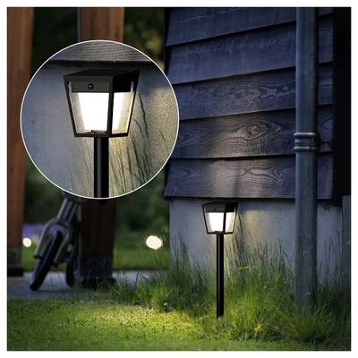 Small outdoor path light glowing beside a house wall, with a circular inset showing a close-up of the lamp.