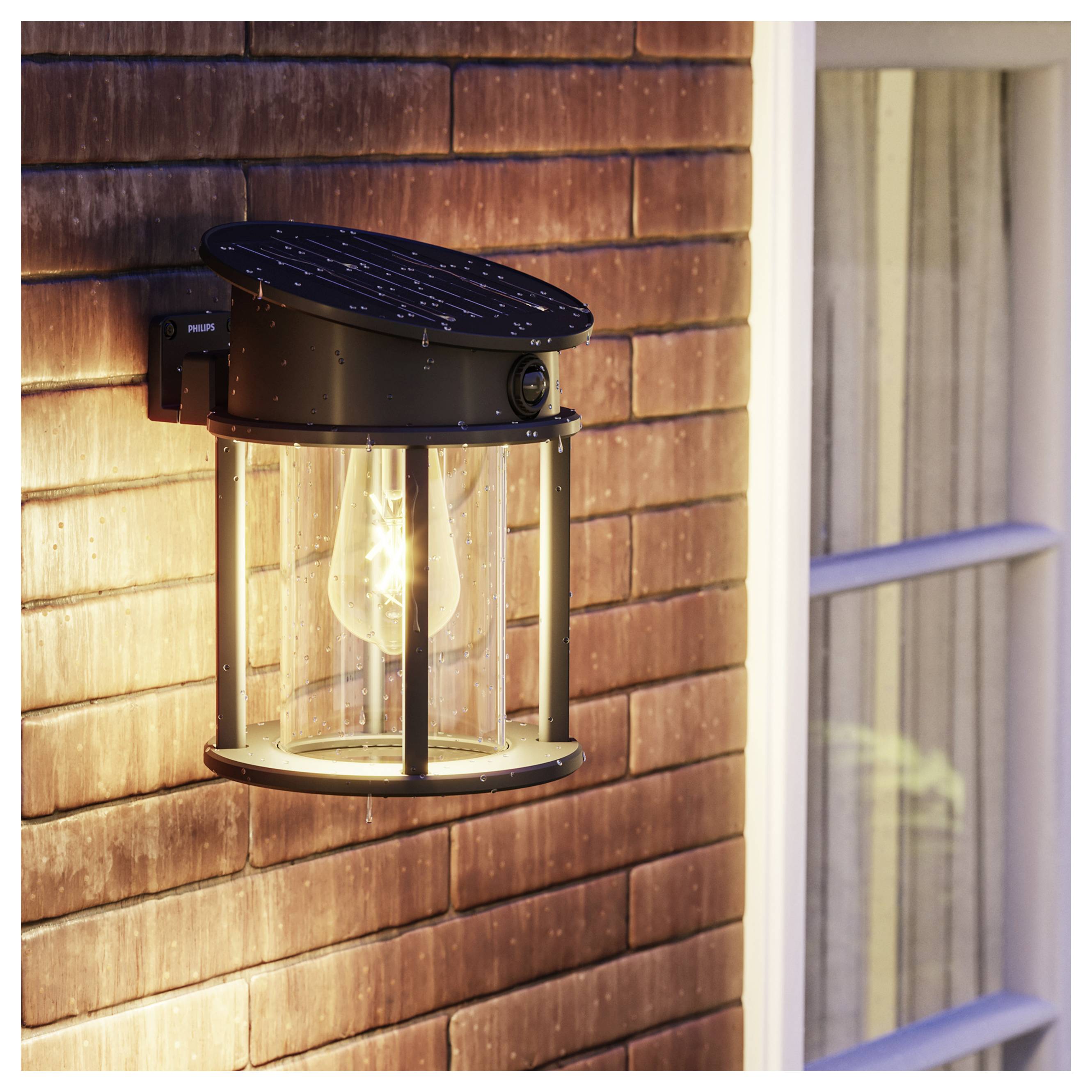 Black outdoor wall lantern with a glowing bulb mounted on a shingled house wall beside a window.<br>