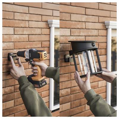 Person installing exterior wall lights on a brick house, using a drill and holding a lantern-style fixture near a window.<br>