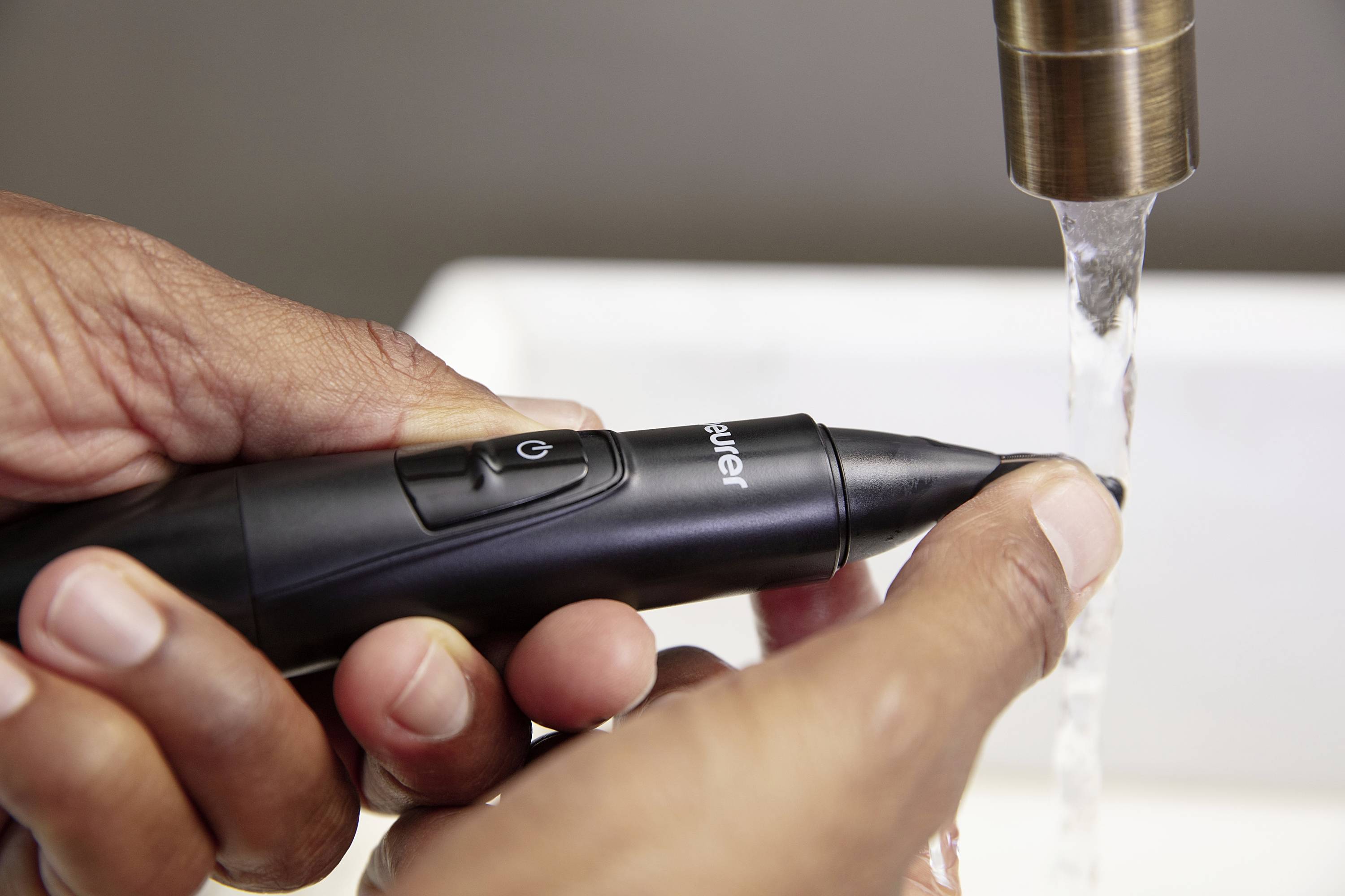 A person is holding an electric razor under running water to clean it.