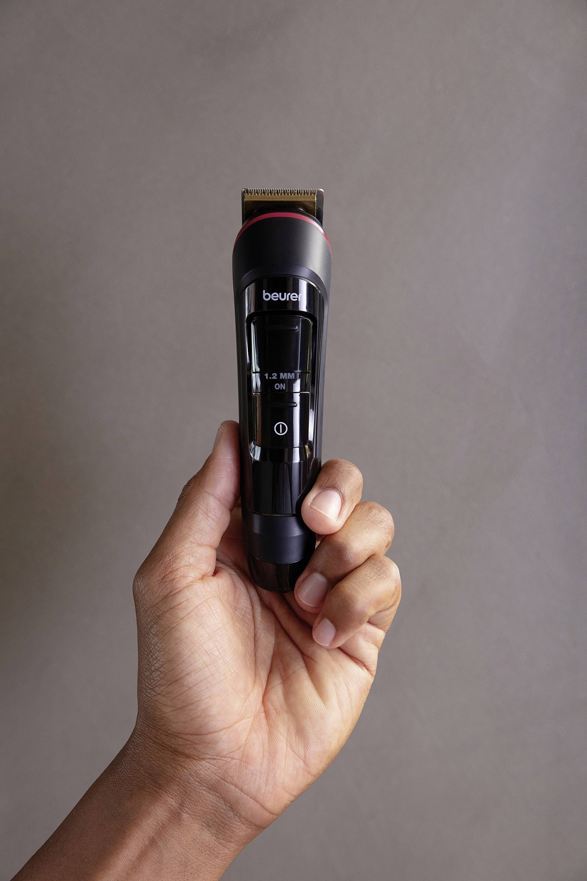A hand is holding a black electric trimmer with the 'beurer' inscription. The background is neutral.