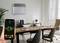 Office with a desk and chairs, with a heating device mounted on the wall in the background. A hand is holding a smartphone with an open heating app on the screen.