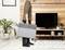 A person is carrying a grey radiator in a modern living room with wooden panelling and a television.