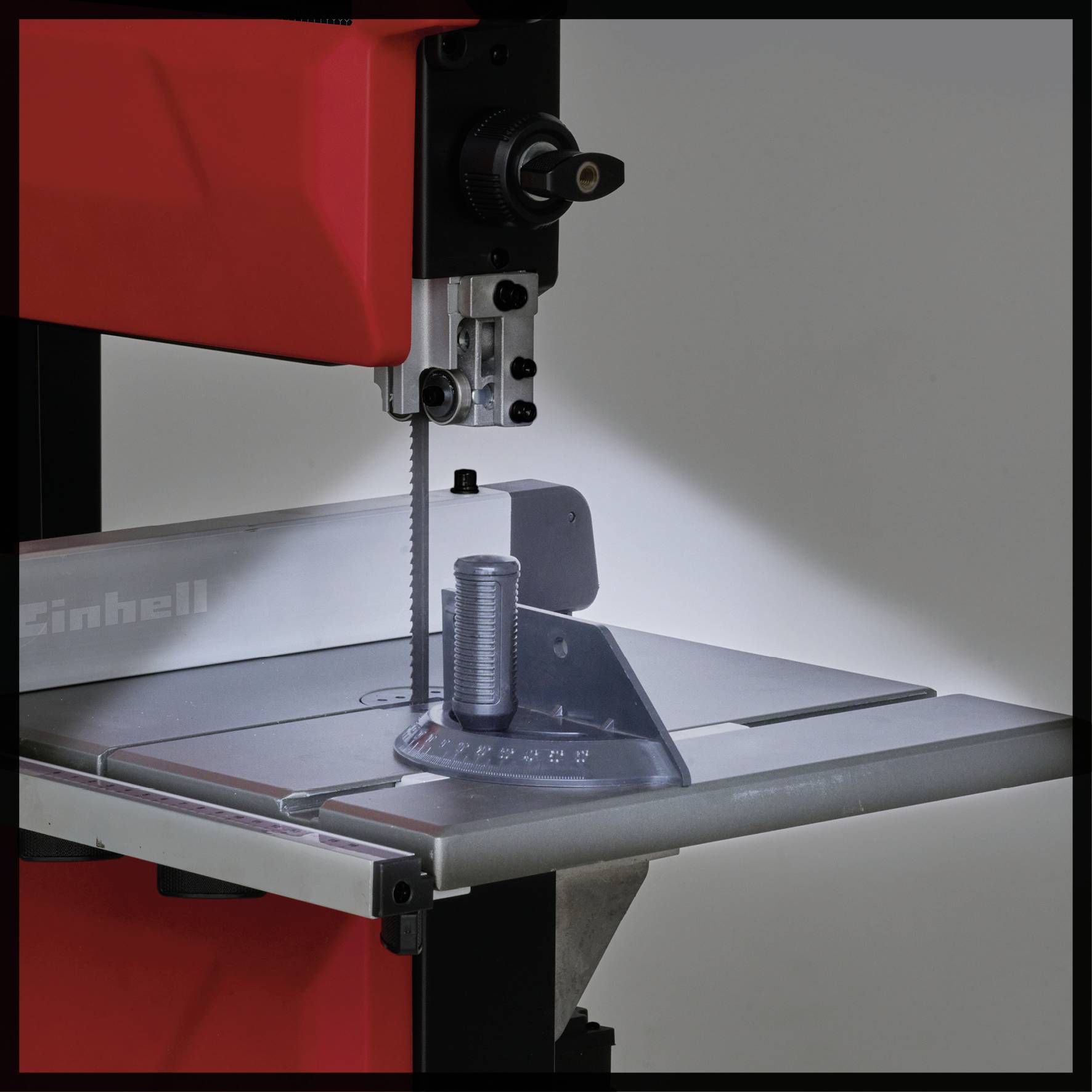 Band saw with a red casing in a workshop. Saw blade vertical, metal mounting table underneath.