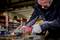 A man in protective clothing and safety glasses grinds metal with an angle grinder in a workshop. Sparks are flying off the metal.