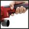 A hand is gripping a red electric angle grinder by its handle, poised to switch on. The thumb is positioned on the power button.