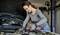 A woman is repairing a car tyre in a workshop. She is wearing safety glasses and gloves and using a tool.