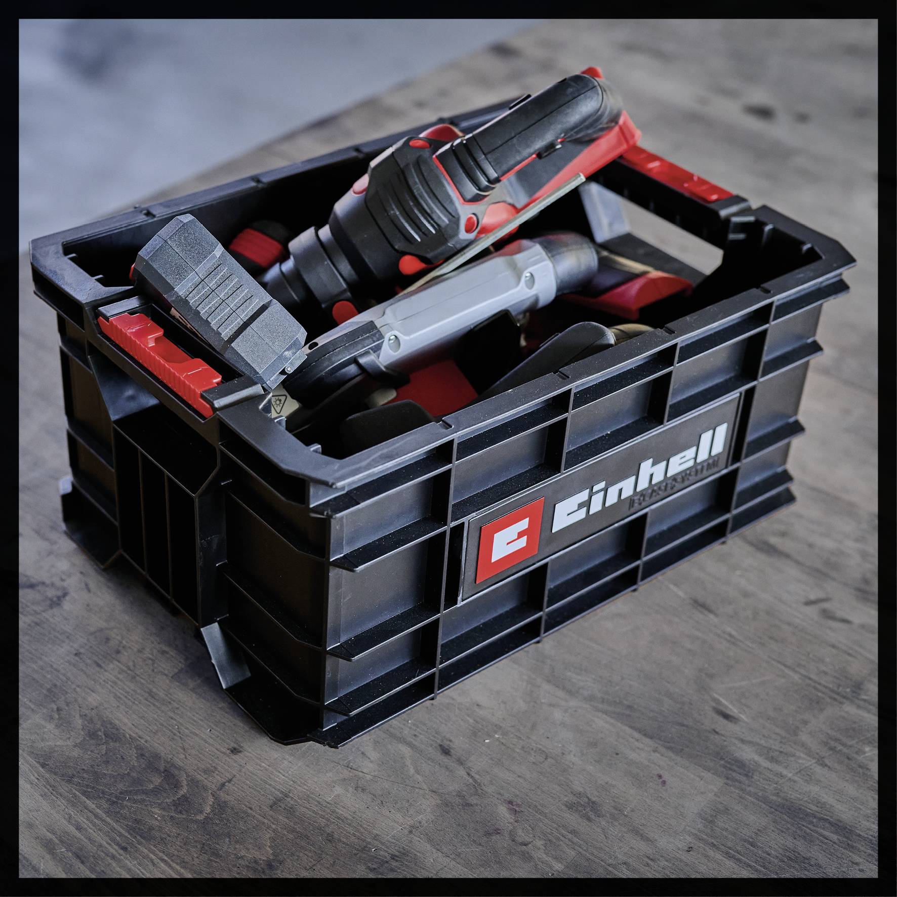 A black plastic box with red and grey electric tools on a wooden table.