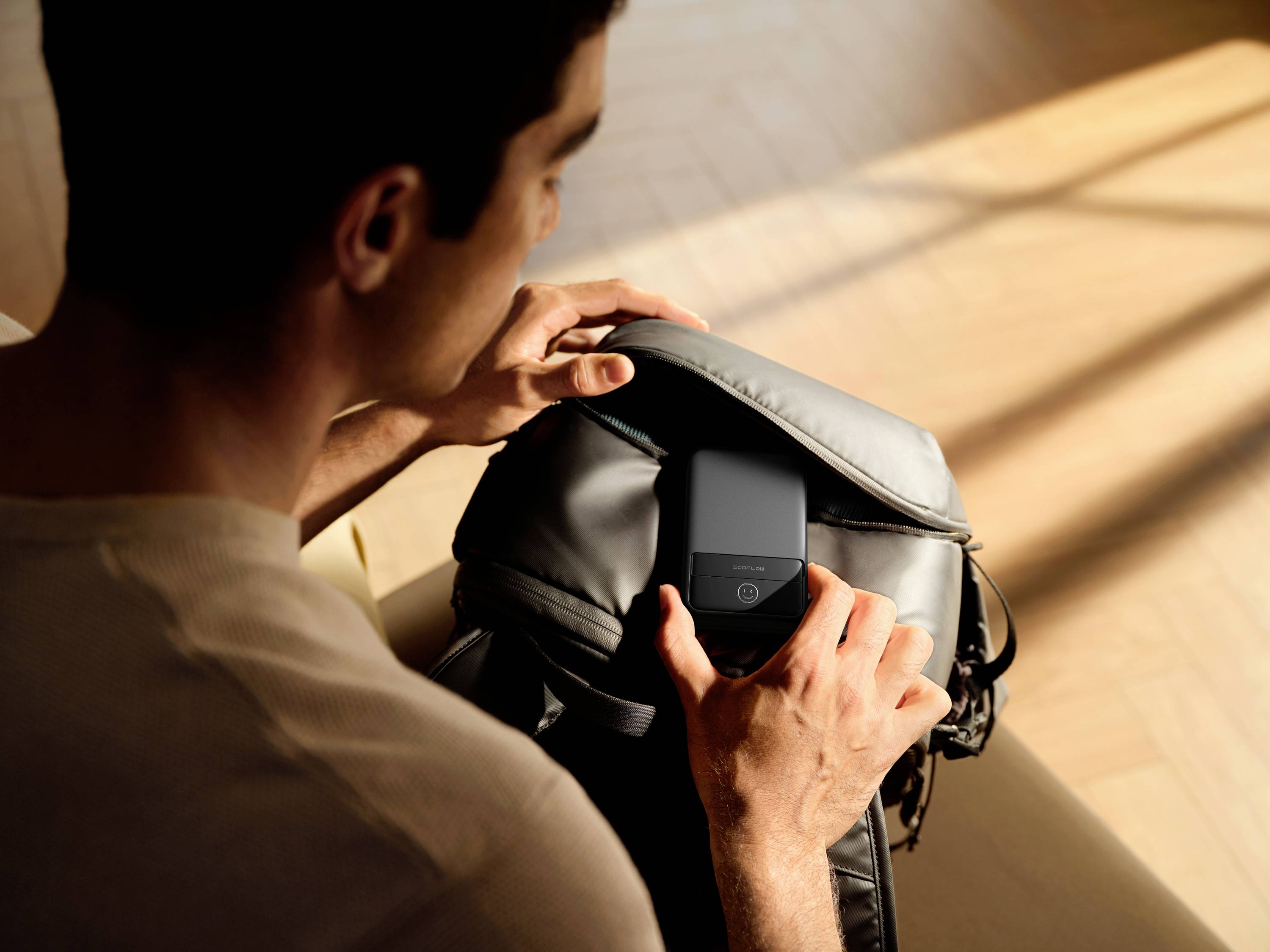 A person opens a rucksack to take out a mobile phone. The light in the room is warm and soft.