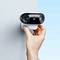 A hand holds a small, dual-lens security camera mounted on a wall, against a blue background.