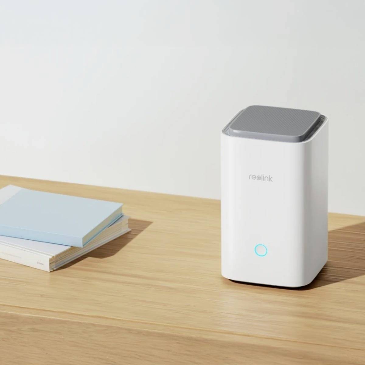 A white, rectangular device with a small blue light ring on a table, next to a stack of blue and white books.