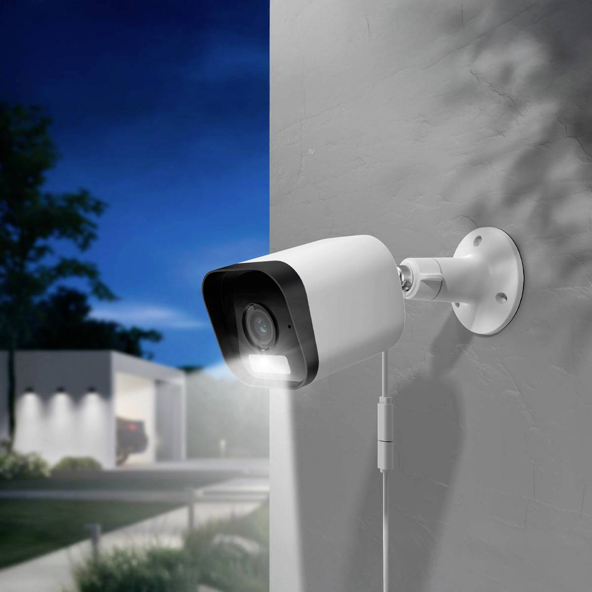 Security camera mounted on a wall, outdoors at dusk. A driveway with a parked car is visible in the background.