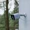 A surveillance camera is mounted on a pole. It is raining, and blurred trees can be seen in the background.