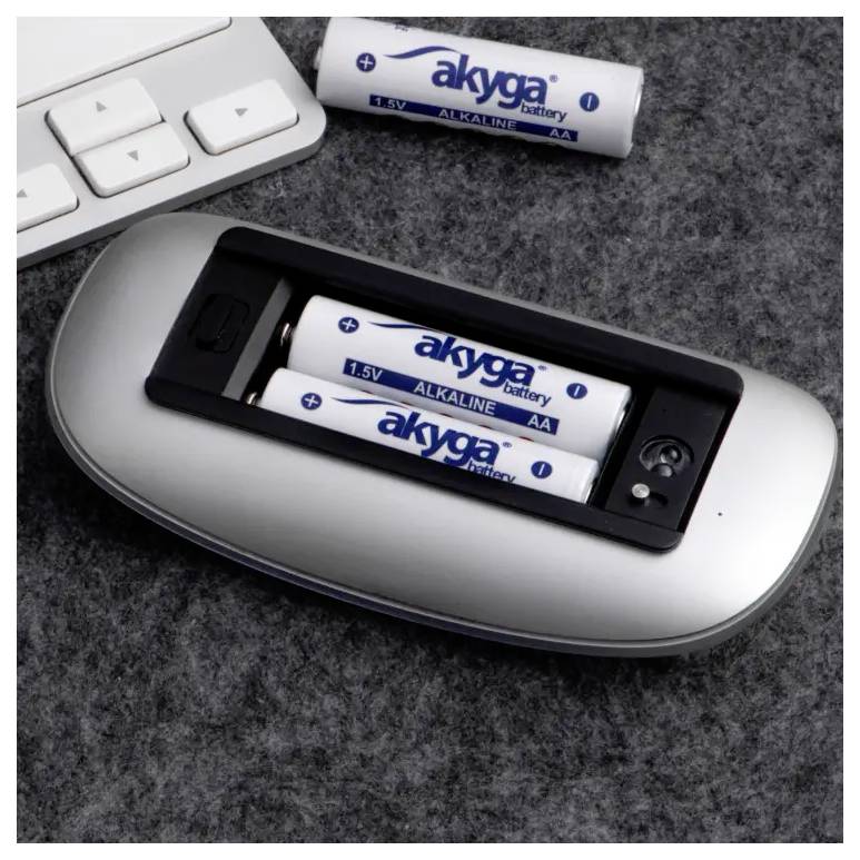 Wireless mouse opened, showing two inserted AA alkaline batteries on a grey background next to a computer keyboard.