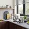 Kitchen worktop with a mixer and accessories, saucepans on shelves and a window with a view of greenery. Cosy kitchen scene.