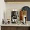 An espresso machine on a kitchen worktop, surrounded by coffee beans, glasses, and a coffee cup.