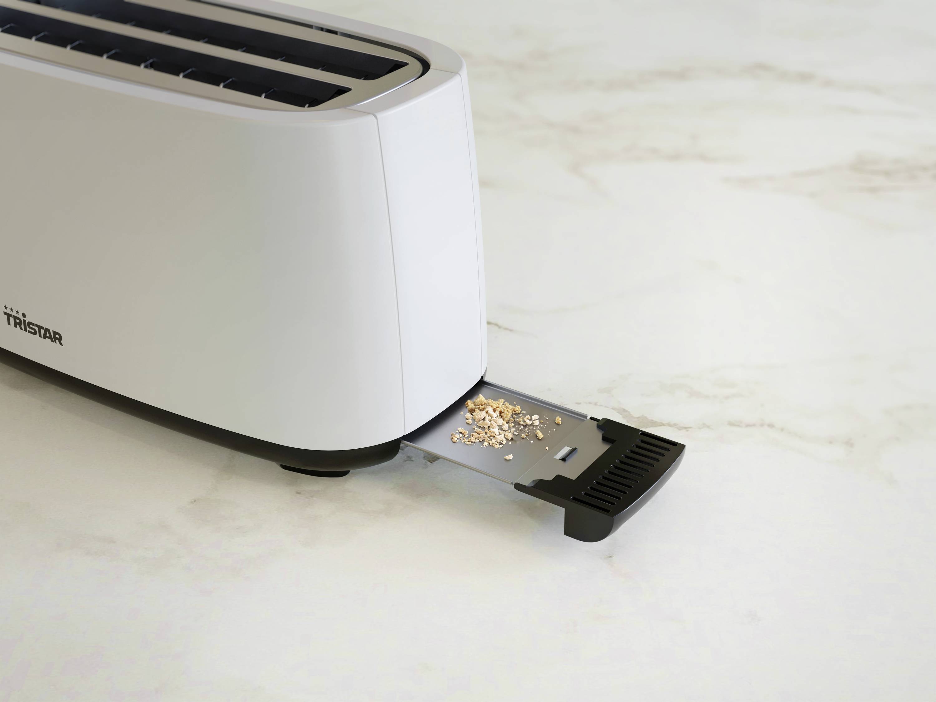 A toaster sits on a worktop with its crumb tray pulled out. A few crumbs are resting on the tray.