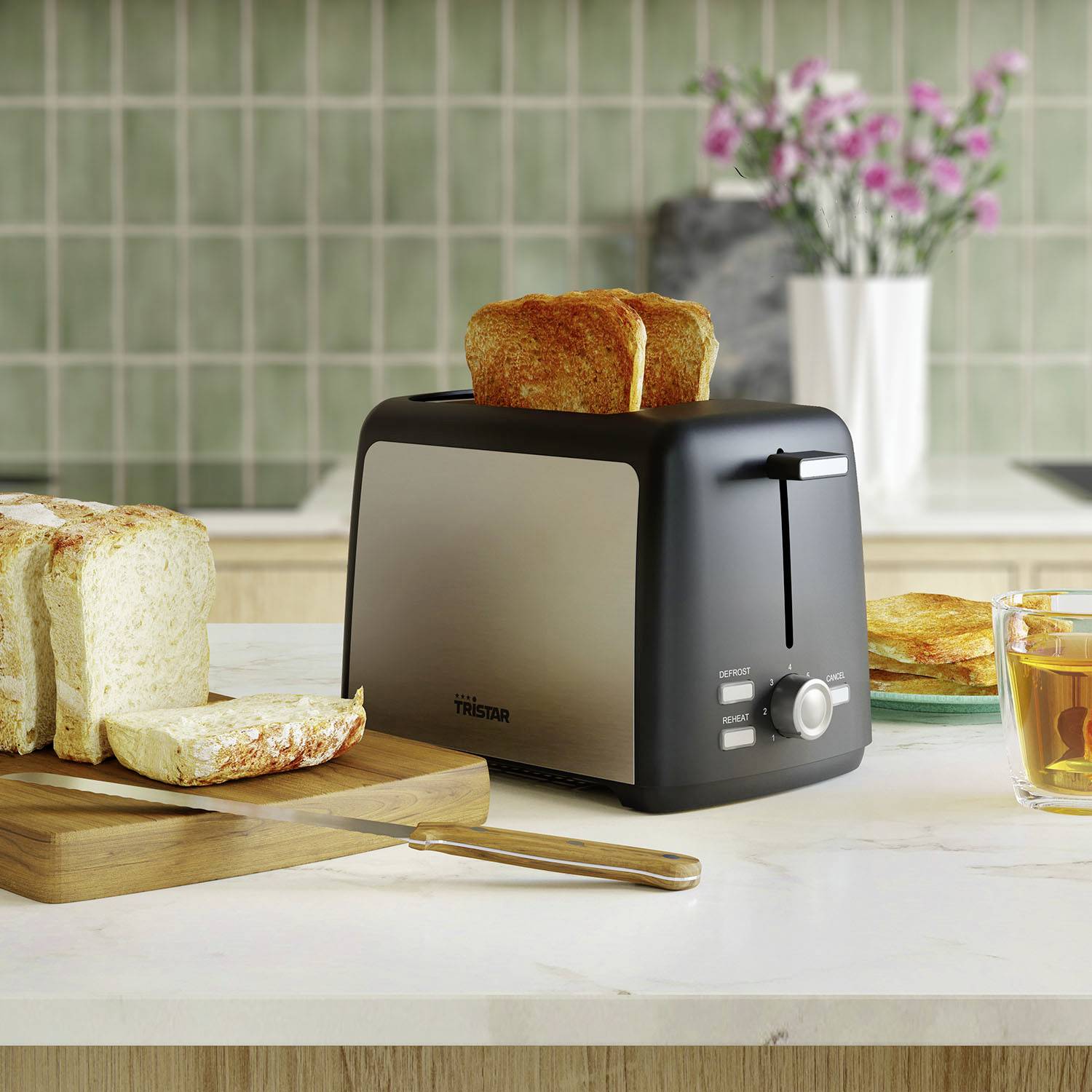 A toaster on a kitchen worktop, toasting two slices of bread. Beside it are sliced bread and a cup of tea.