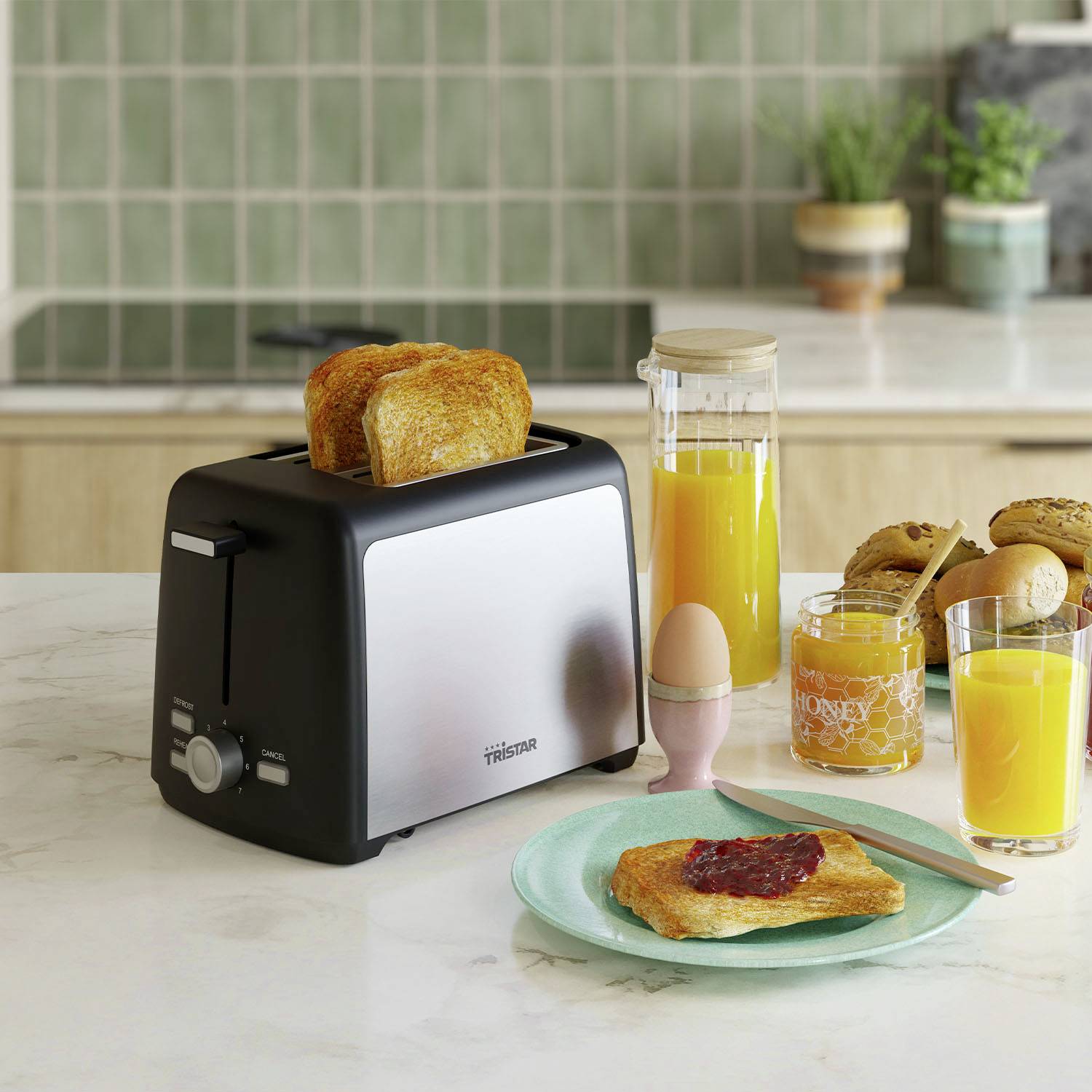 A toaster with two toasted slices of bread sits on a kitchen worktop next to a glass of orange juice and a jar of jam.