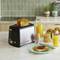 A toaster with two toasted slices of bread sits on a kitchen worktop next to a glass of orange juice and a jar of jam.