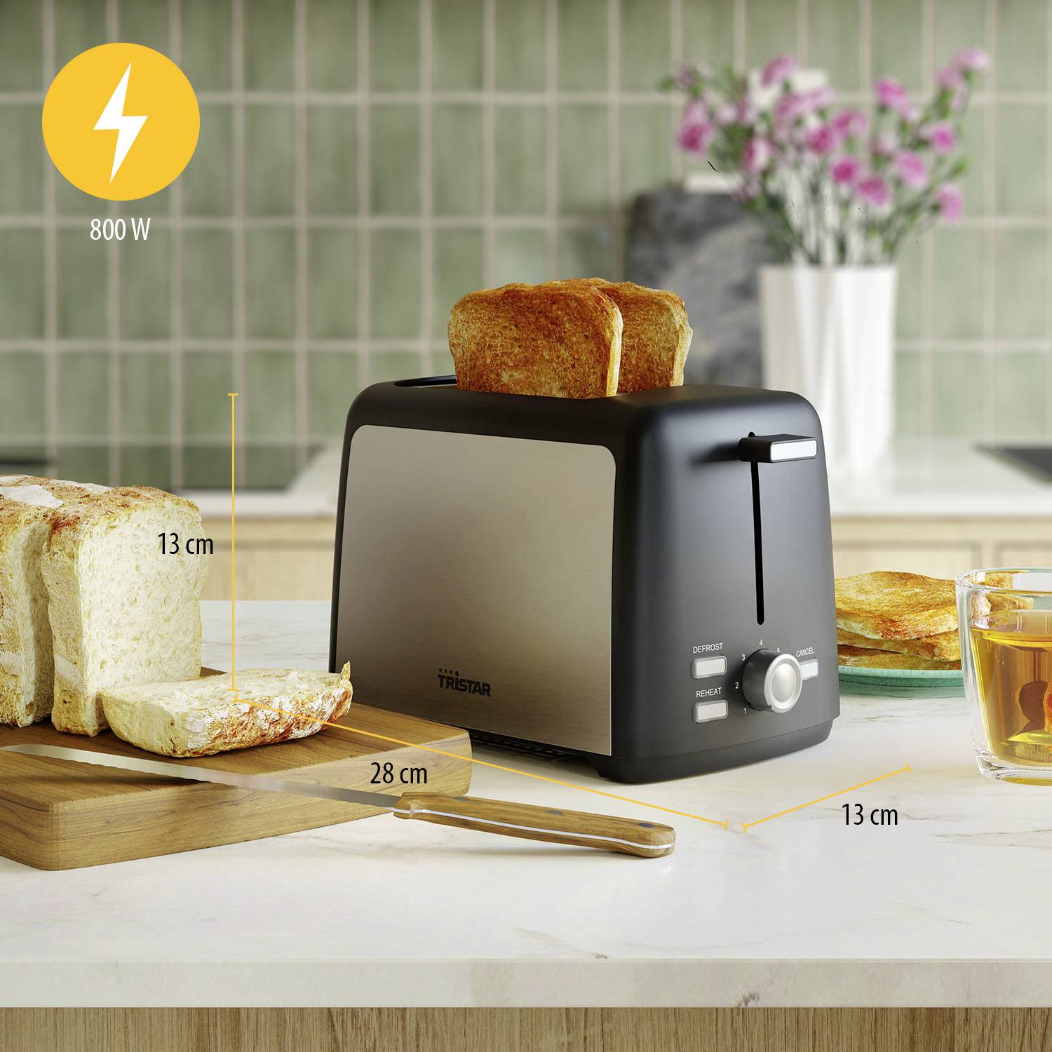 A toaster with two toast slots on a kitchen worktop. A knife is beside it, with bread and a cup of tea visible.