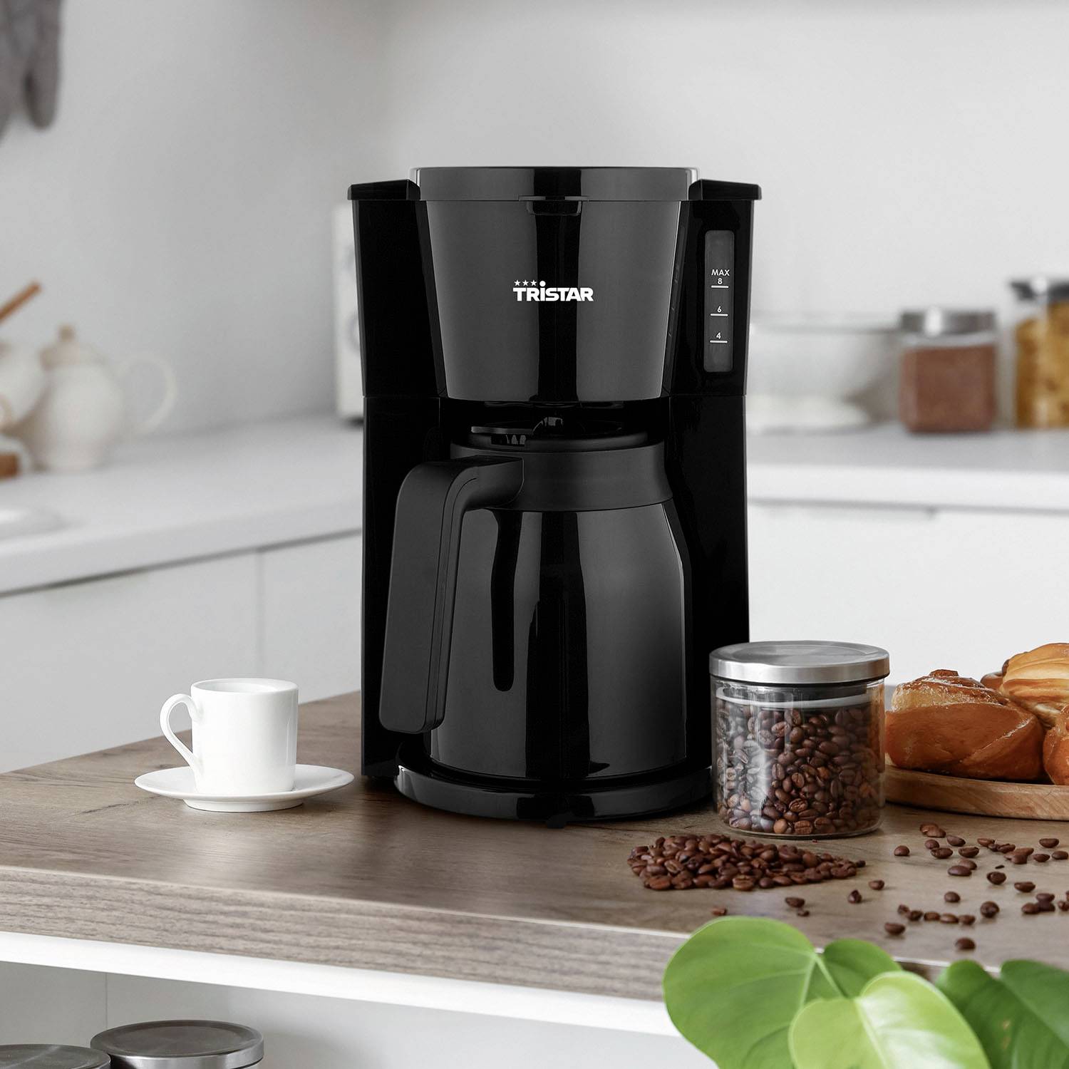 A black coffee machine with a glass carafe sits on a kitchen worktop, surrounded by coffee beans and cups.