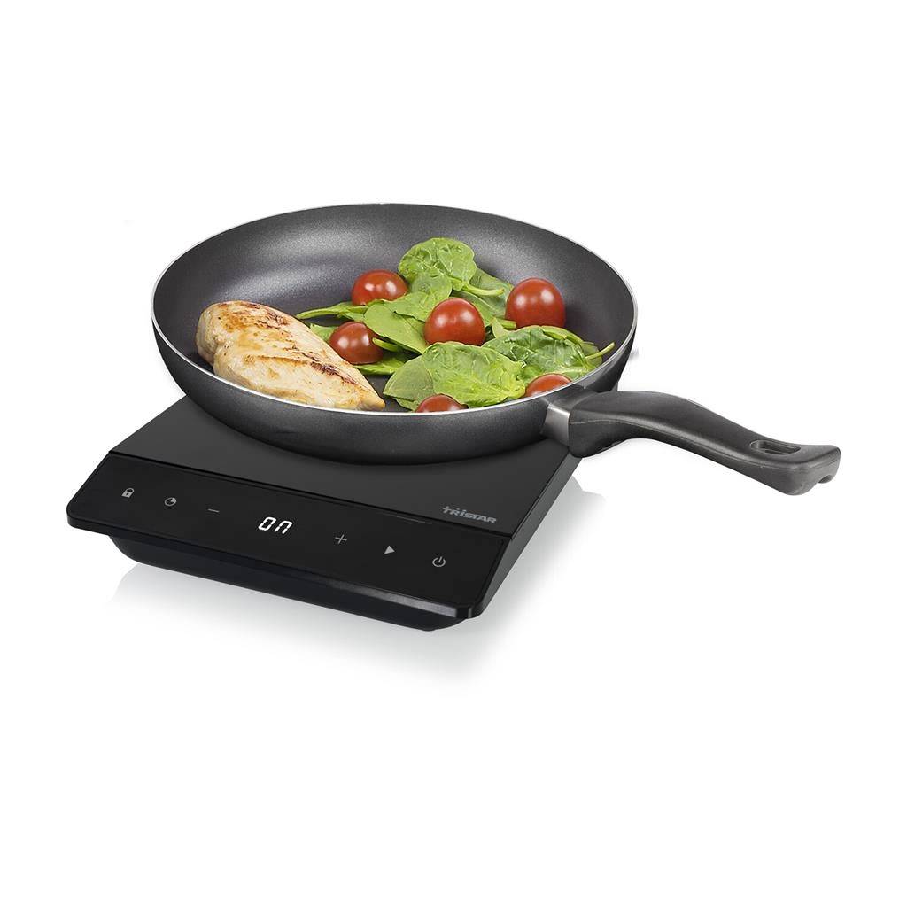 A pan on a portable hob with chicken breast, spinach, and tomatoes. The hob displays 'On' on its screen.