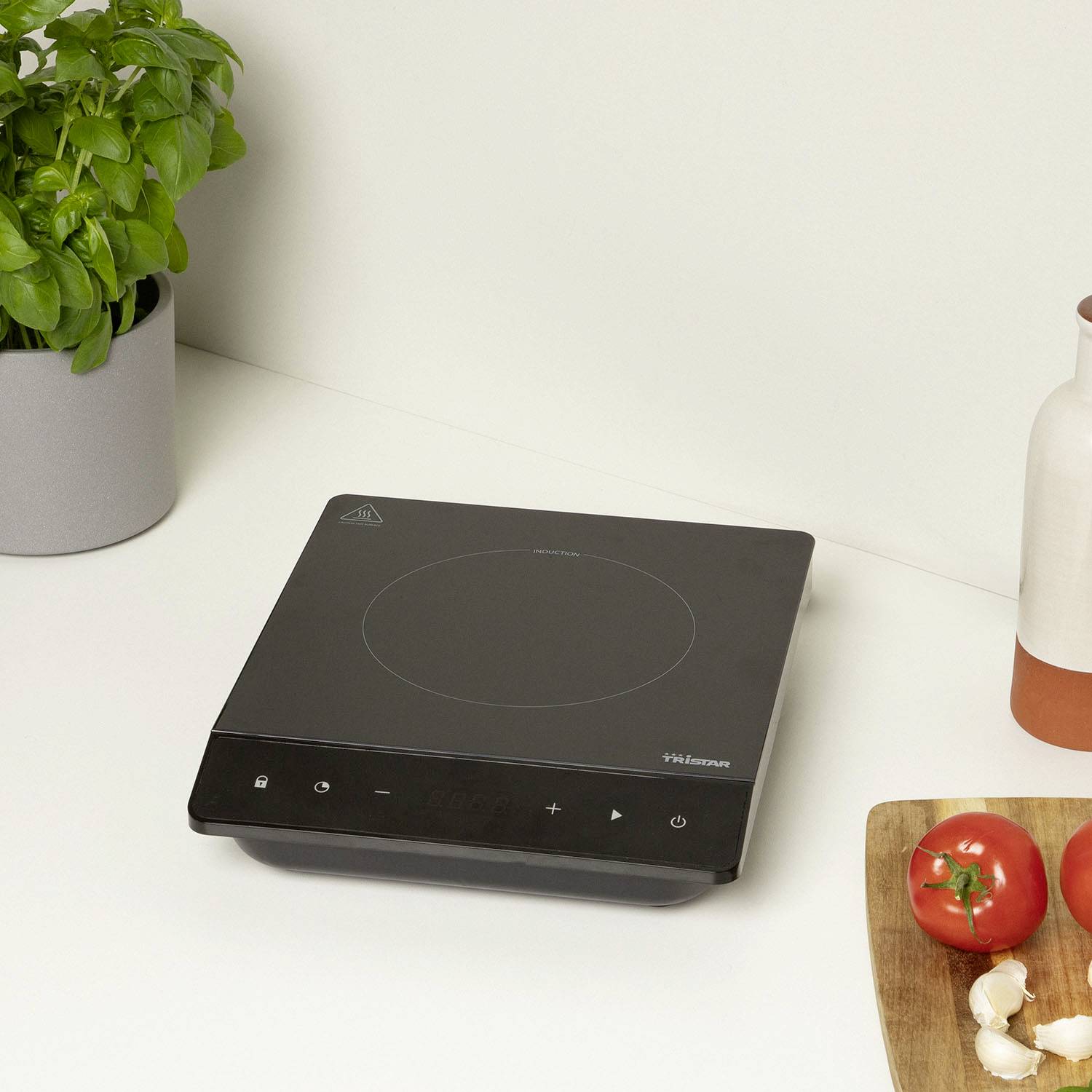 An induction hob on a white worktop next to a plant and chopped vegetables.