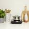 A pot on a modern induction hob, surrounded by kitchen decor: a plant pot, a utensil holder, and bottles.