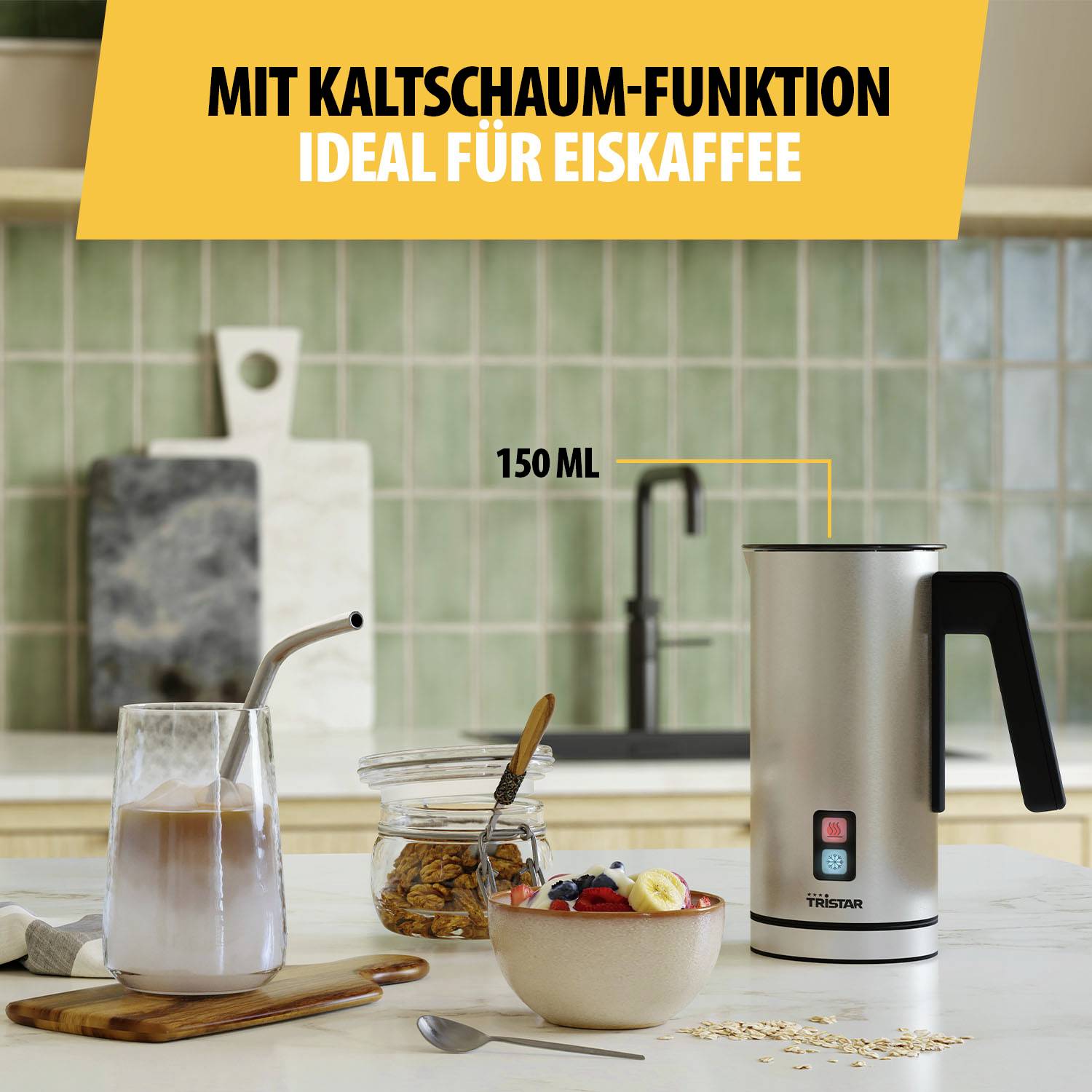 Electric milk frother on kitchen table, beside a glass of iced coffee with a straw, a bowl of muesli and pieces of cheese in the background.