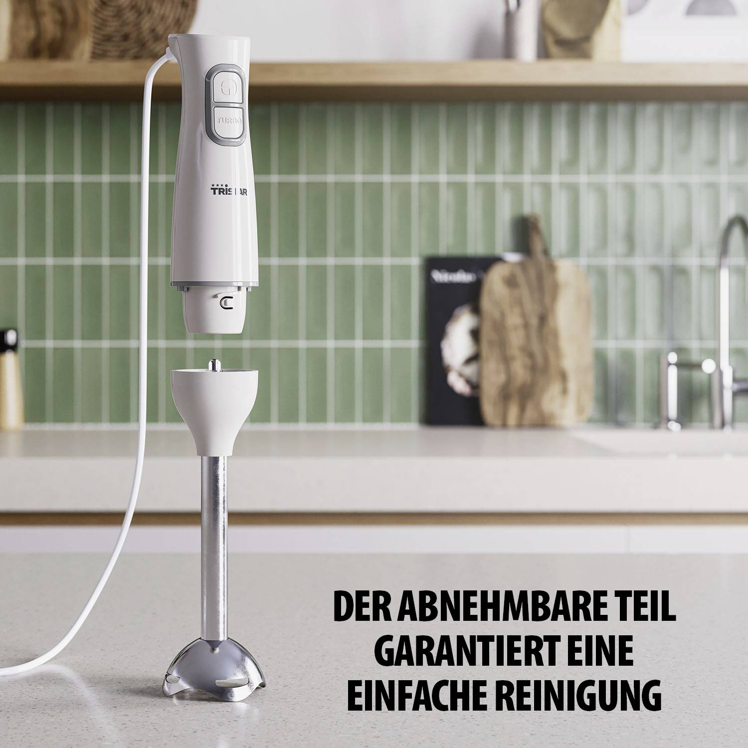 A white hand blender is standing on a kitchen worktop in front of green tiles. Text on image: 'The detachable part ensures easy cleaning'.