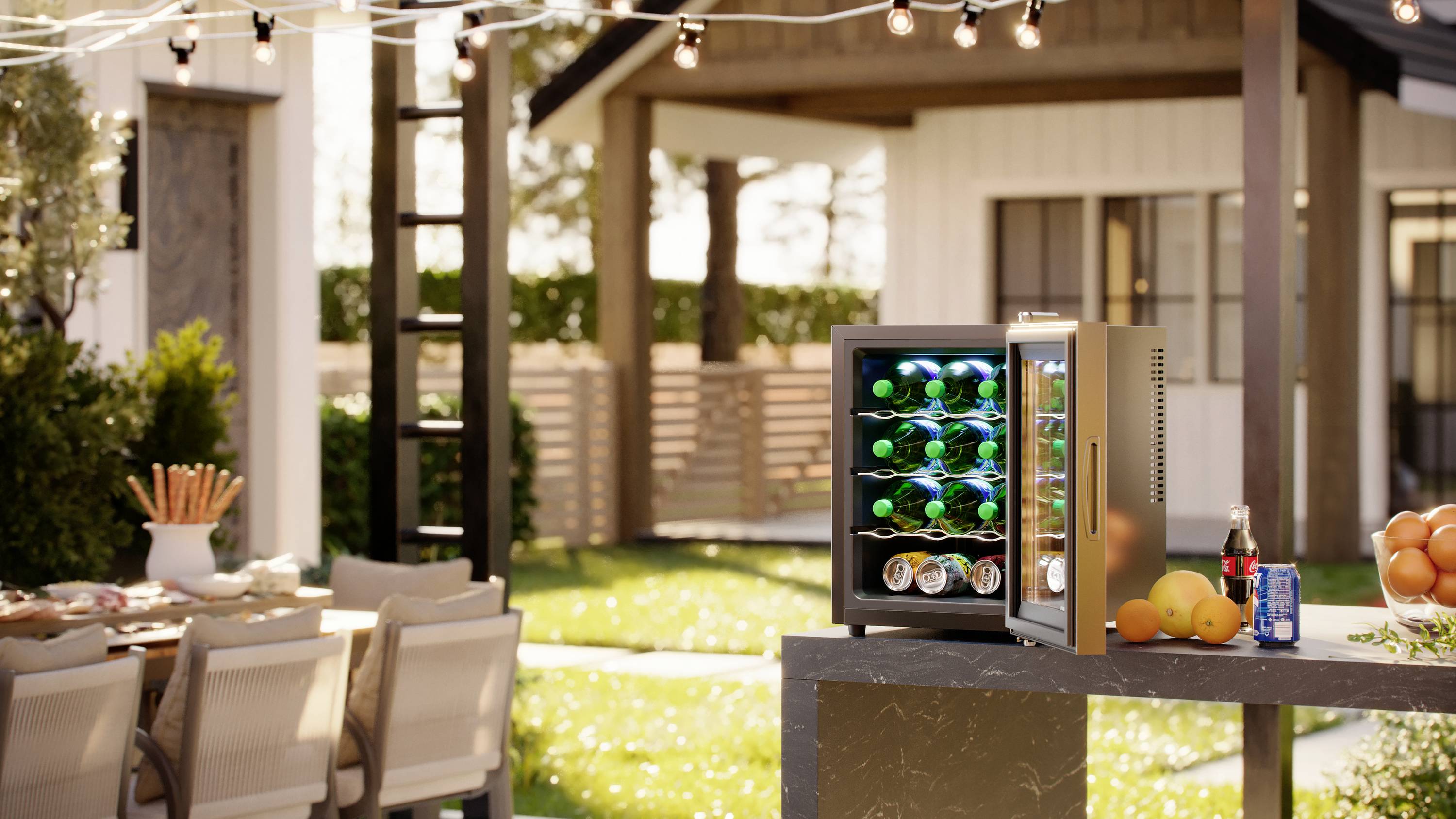 An open drinks fridge with wine bottles and cans is standing on a table in a sunny garden next to a small cottage; party preparations.