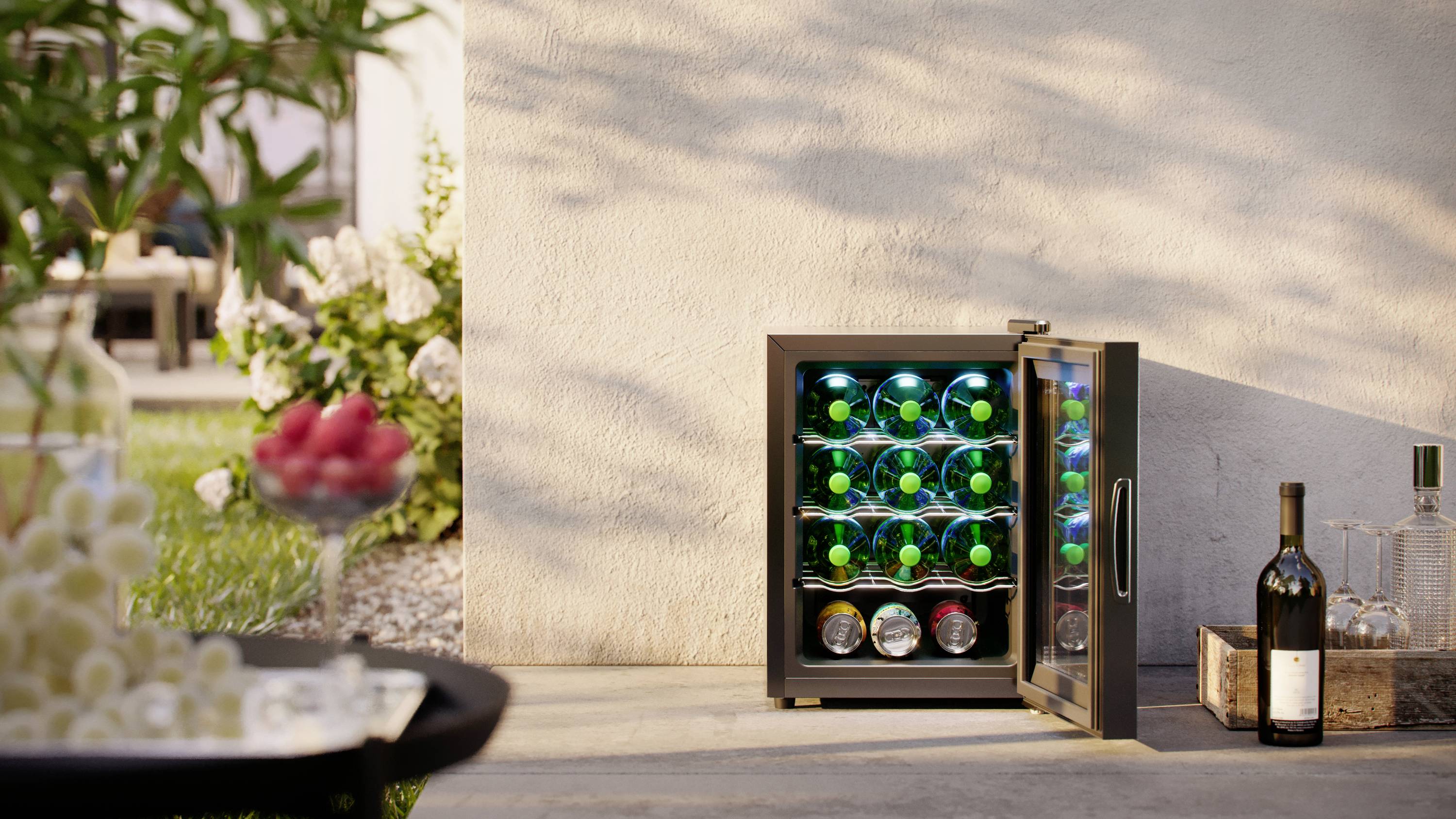An opened wine fridge outdoors with green and blue illuminated bottles, alongside a bottle of red wine and glasses.