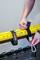 A person is attaching a yellow tool storage rack to the wall using a black hook-and-loop fastener and carabiner.