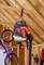 A red leaf blower device hangs on a wooden frame in a garage. Beneath it, a blue bicycle and gardening tools.