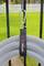 A white, spiral-shaped hose is secured to a black fence with a hook-and-loop fastener and a carabiner clip. Grass is visible in the background.