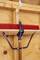 A red broom hangs on the wooden structure of a garage, secured with a metal hook and a black strap.