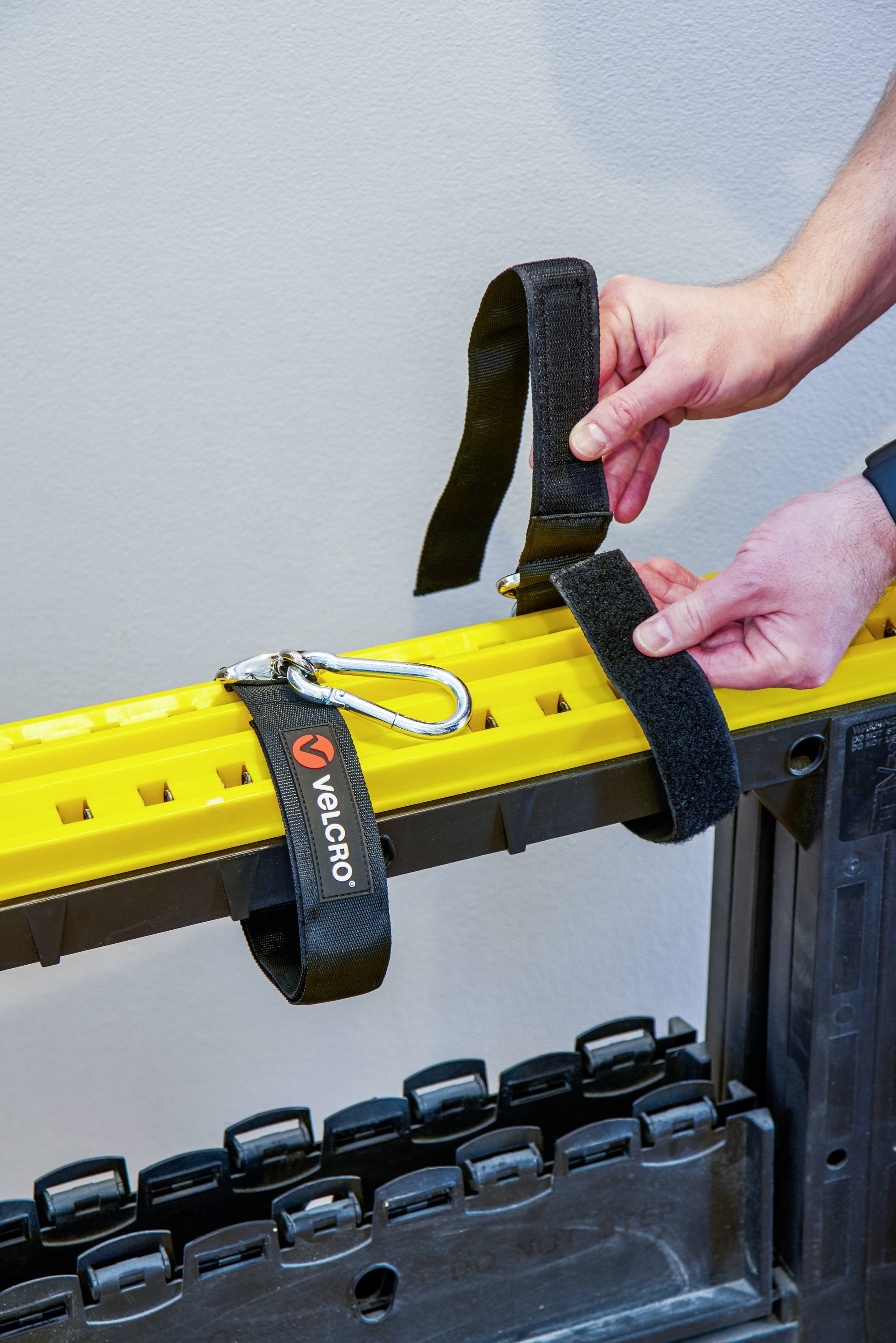 A person is attaching a yellow cable trunking to a black frame using hook and loop fasteners and a carabiner for secure attachment.