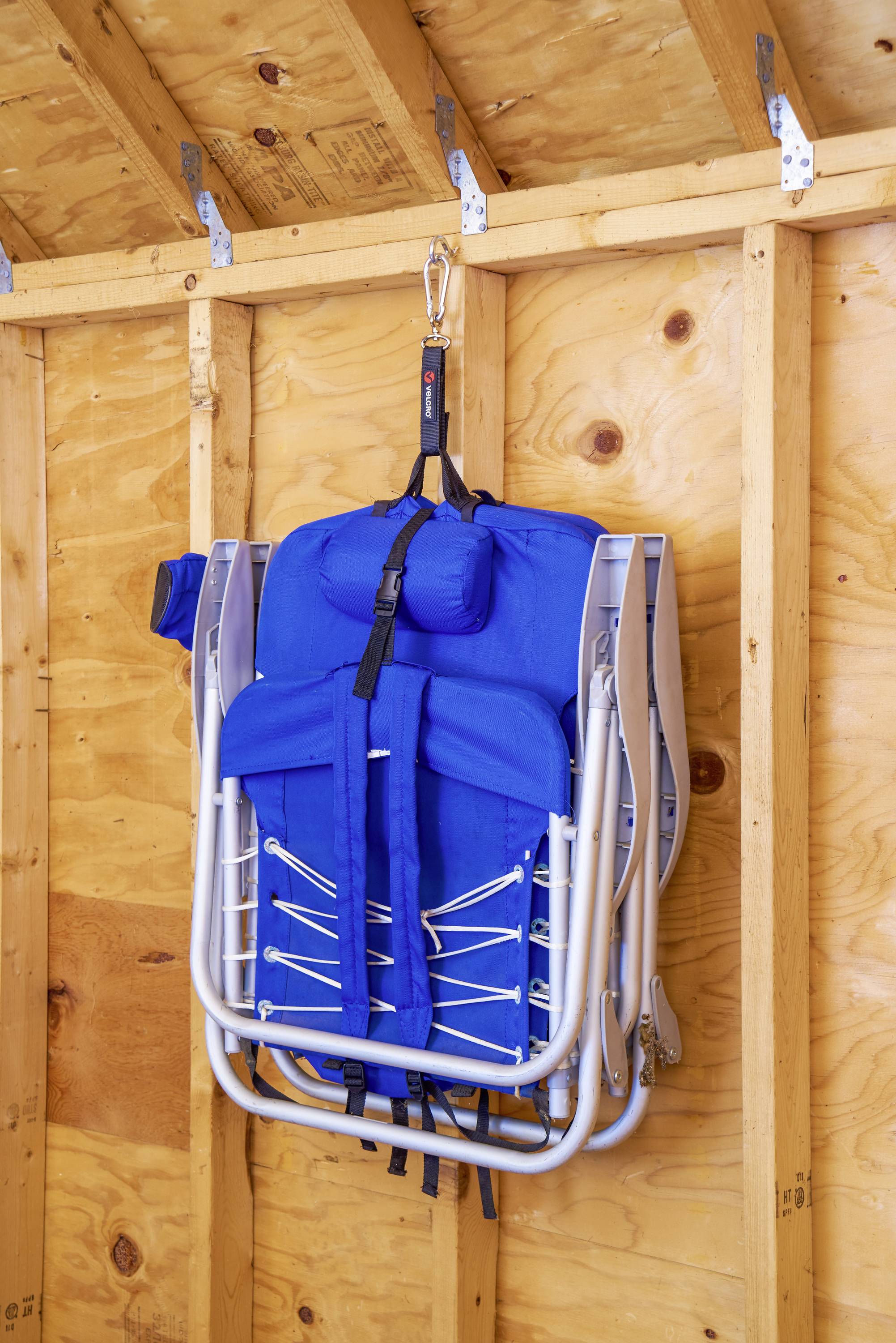 A blue folding chair hangs on a hook on the wall in a wooden shed. The room has a wooden interior wall.