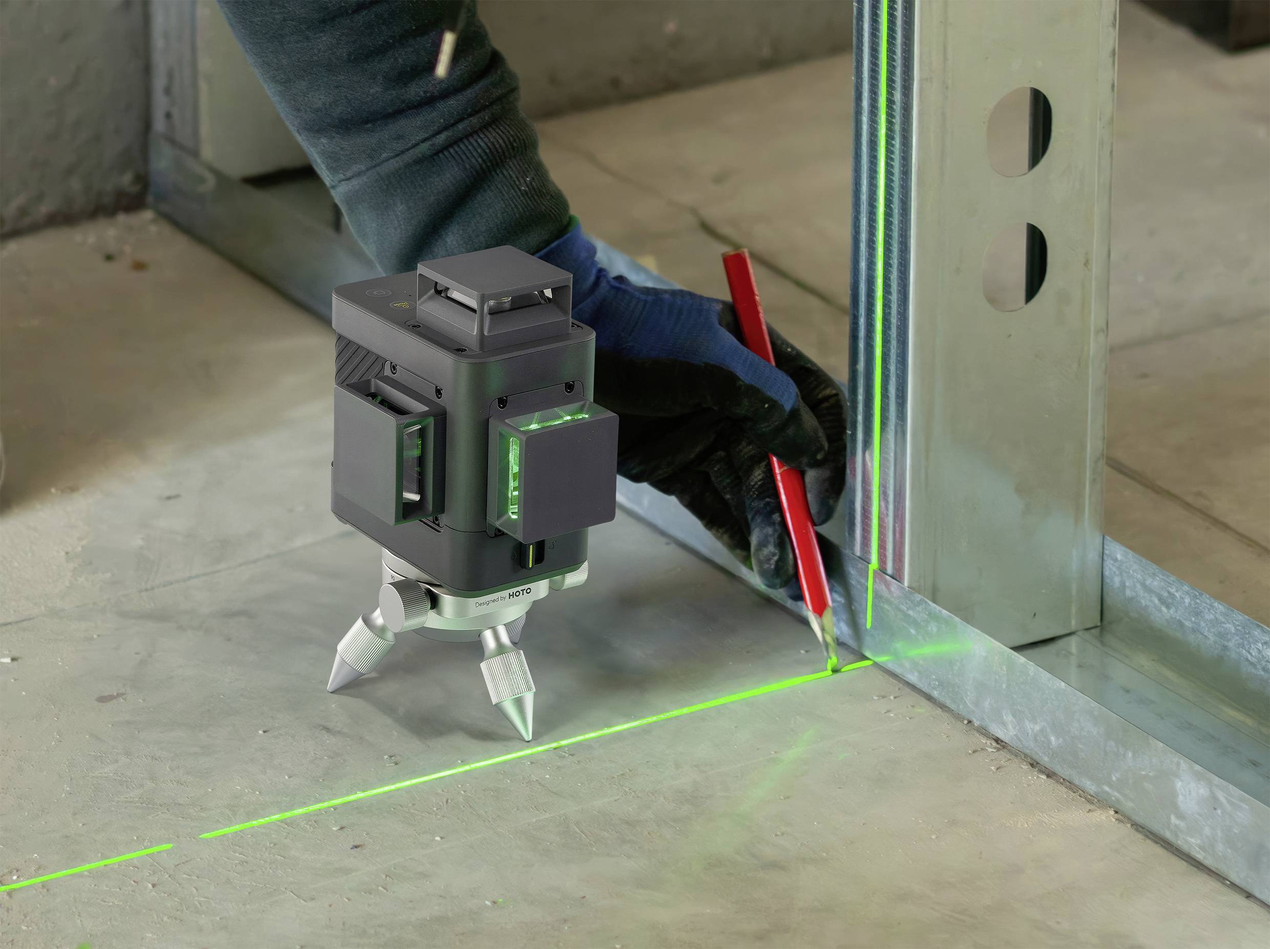 A craftsman is using a green laser level to align a wall structure. He is marking precisely with a red pen.